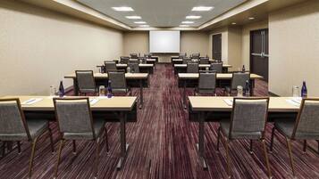A conference room with multiple tables and chairs, a projector screen, and a carpeted floor.