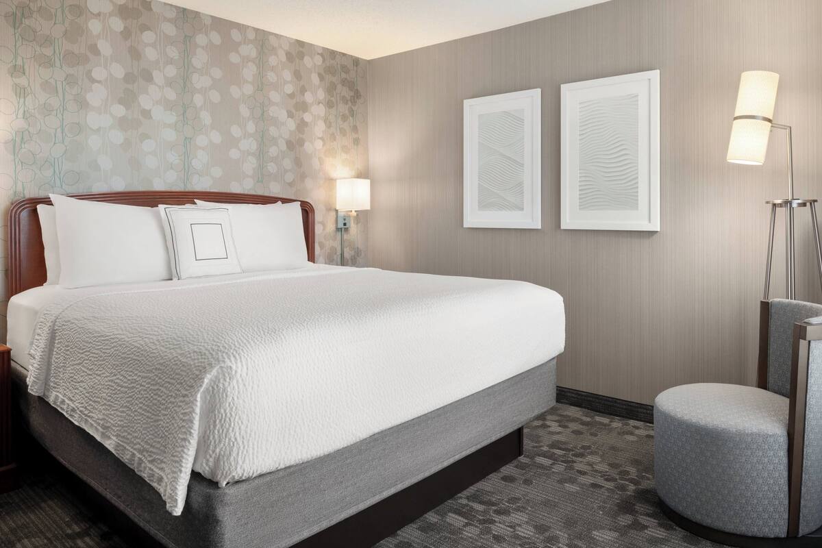 A hotel room with a large bed, a nightstand, a lamp, a chair, and two framed pictures on the wall.