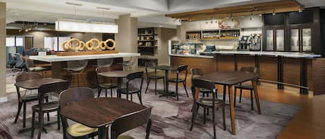 A modern restaurant with a bar area, wooden tables and chairs, and a patterned carpet.