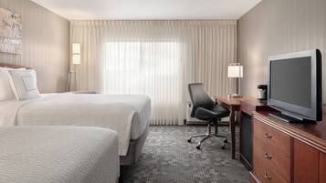 A hotel room with two beds, a desk with a television, a chair, and a dresser.