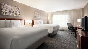 A hotel room with two beds, a desk with a TV, and a chair.