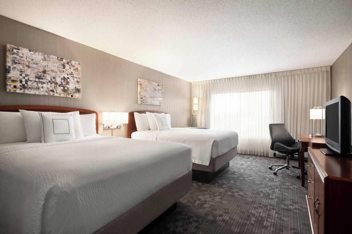 A hotel room with two beds, a desk with a TV, and a chair.