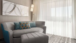 A modern living room with a grey sofa, patterned cushions, a floor lamp, and a large abstract painting on the wall.