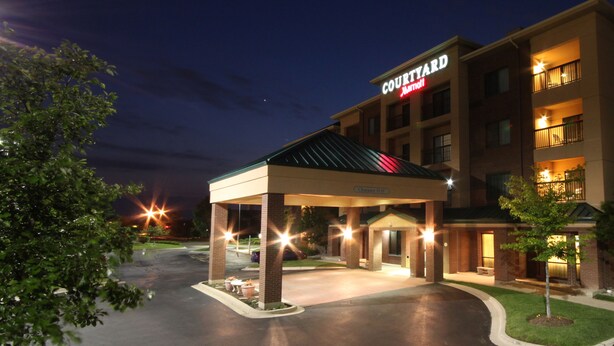 A Courtyard Marriott hotel entrance at dusk with a covered parking area, a clear sky, and a well-lit building facade.