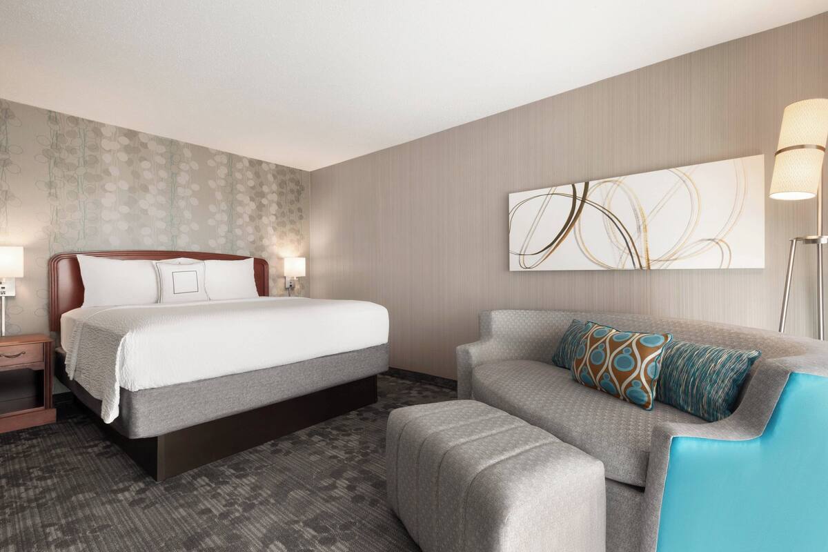 A hotel room with a bed, a sofa, a nightstand, and a lamp.