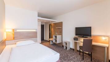 Une chambre d’hôtel avec un lit, un bureau avec une télévision, une chaise et une petite table.