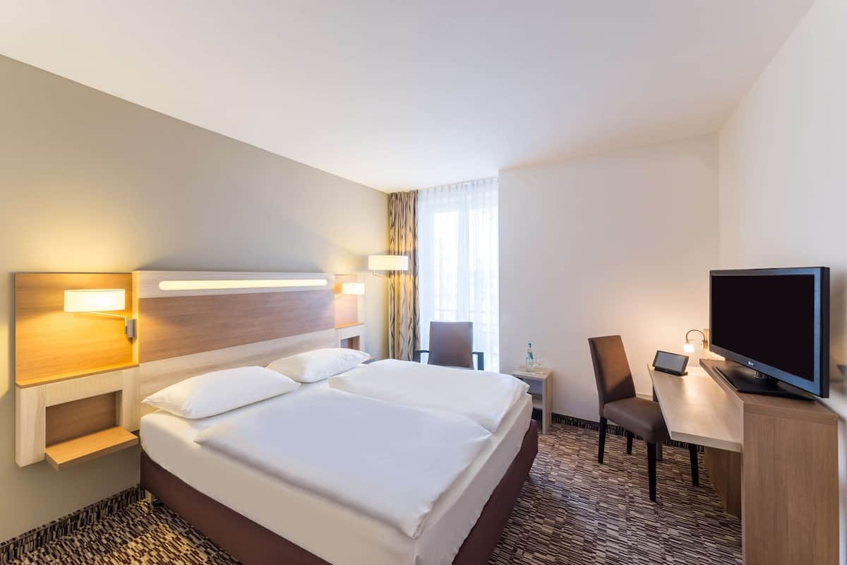 Ein Hotelzimmer mit einem großen Bett, einem Schreibtisch mit Fernseher und einem Sessel.