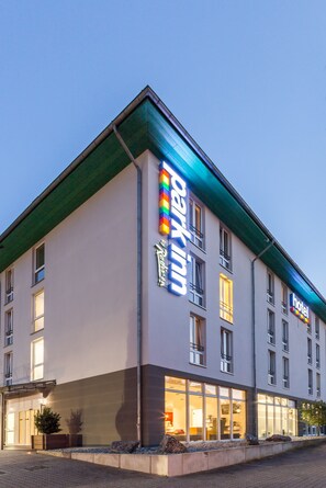 A modern hotel with a prominent sign, large windows, and a well-lit entrance.