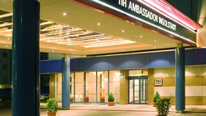 The exterior of NH Ambassador Ingelstadt hotel with a modern design, featuring a prominent entrance and illuminated signage. - NH Ingolstadt (Ingolstadt)