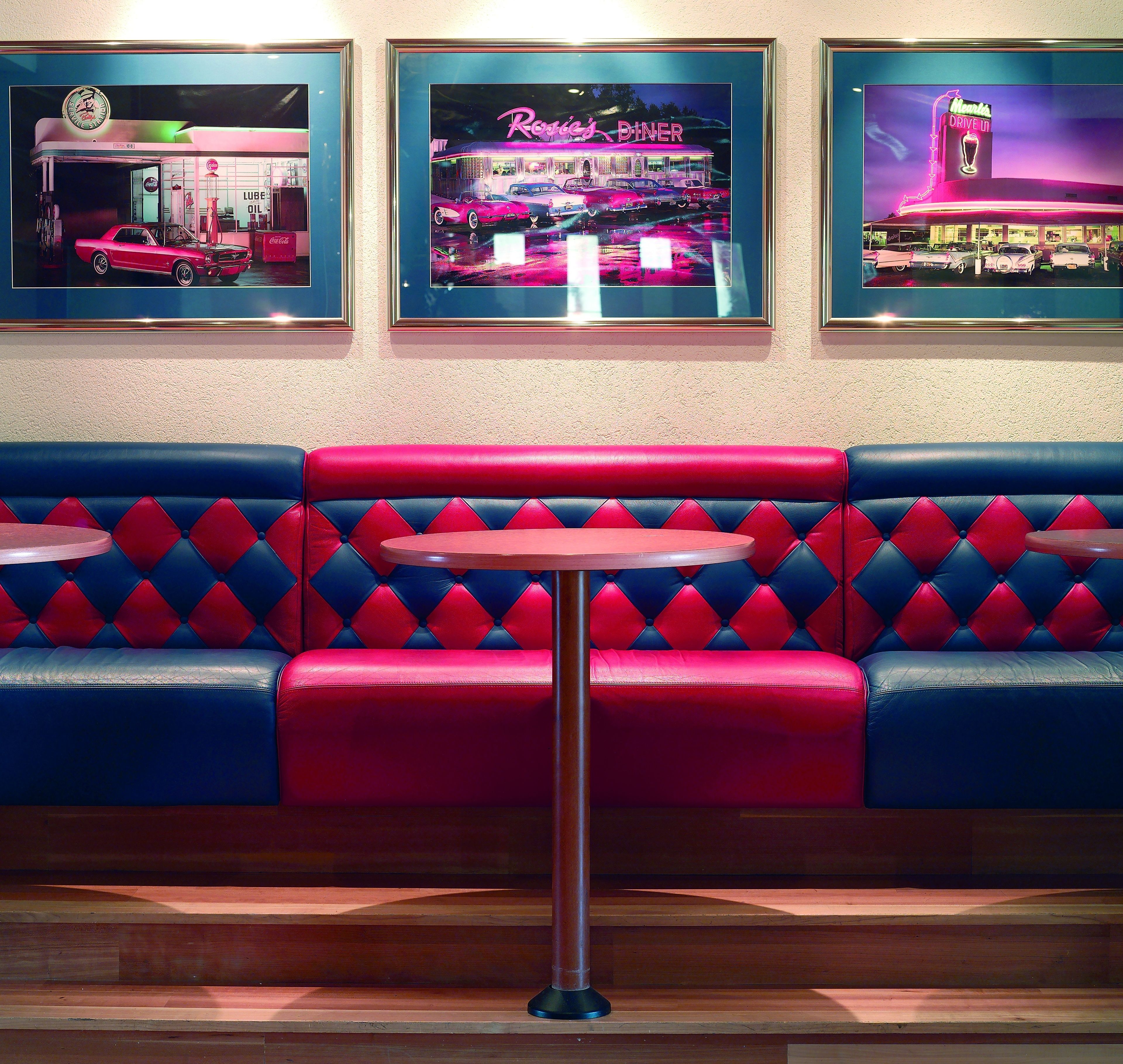 Ein Diner-Interieur mit einer rot-blauen Sitzgruppe aus Sitzecken, einem zentralen Tisch und Neonreklame.