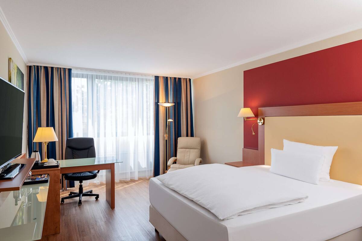 A hotel room with a bed, desk, chair, and a television.