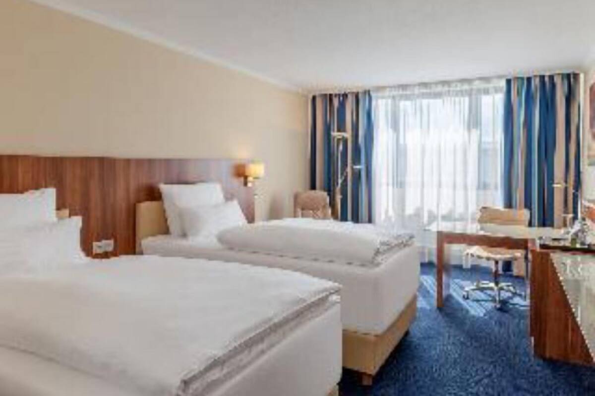 A hotel room with two beds, a desk, a chair, and a view of the city.