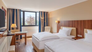 A hotel room with two beds, a desk, a chair, a TV, and a window with curtains. - NH Ingolstadt (Ingolstadt)
