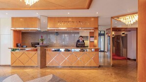 A reception area with a receptionist, a reception desk, and a red carpet leading to an elevator. - NH Ingolstadt (Ingolstadt)