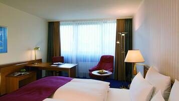 Een hotelkamer met een bed, een bureau, een stoel, een klein tafeltje met eten erop en een lamp.