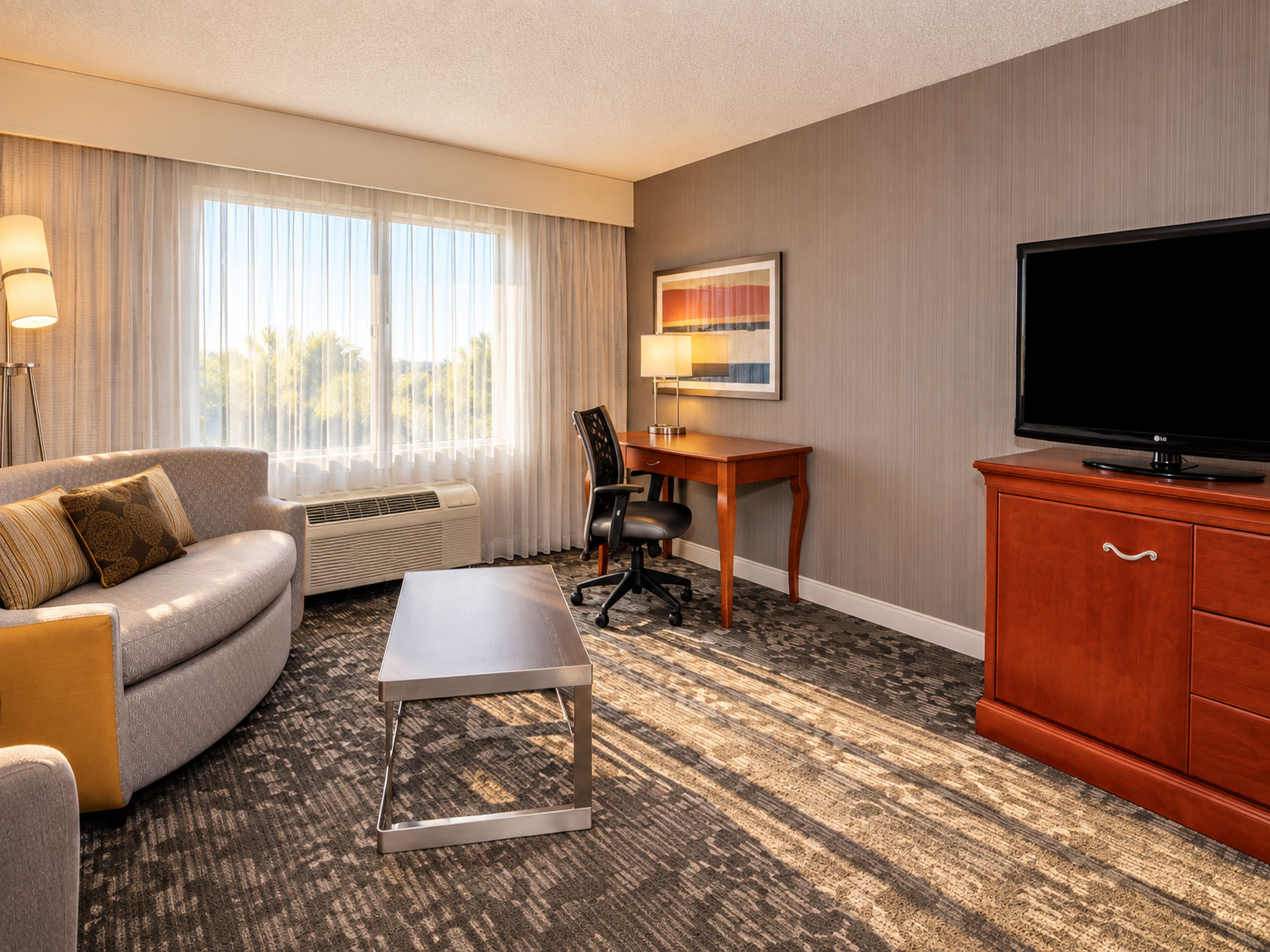 A hotel room with a sofa, a desk, a television, and a painting on the wall.