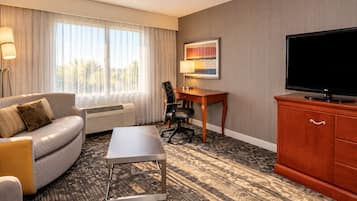 A hotel room with a sofa, a desk, a television, and a painting on the wall.