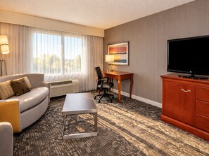 A hotel room with a sofa, a desk, a television, and a painting on the wall. - Courtyard by Marriott Newark Silicon Valley (Newark)