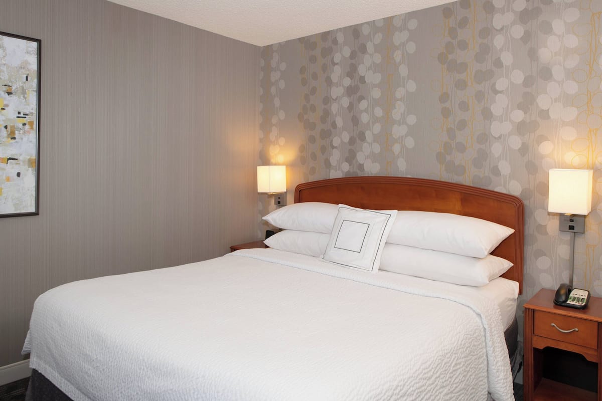 A neatly made bed with a wooden headboard, two bedside lamps, and a framed picture on the wall.