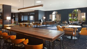 Un hall d’hôtel moderne doté de plusieurs espaces de détente, notamment une longue table commune et plusieurs petites tables accompagnées de chaises.