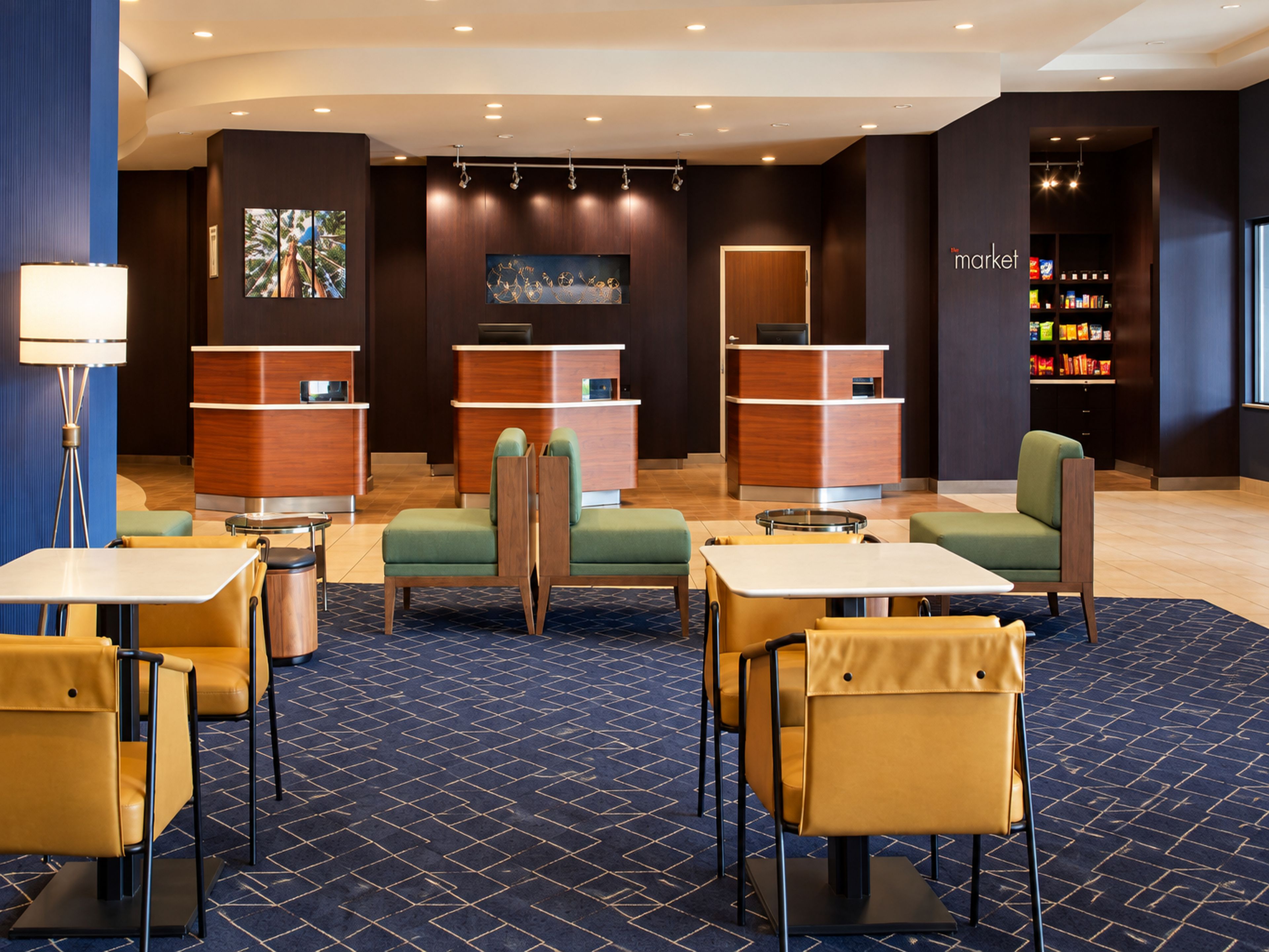 Hall dell'hotel con reception, aree salotto e una macchina distributrice con l'insegna 'market'.