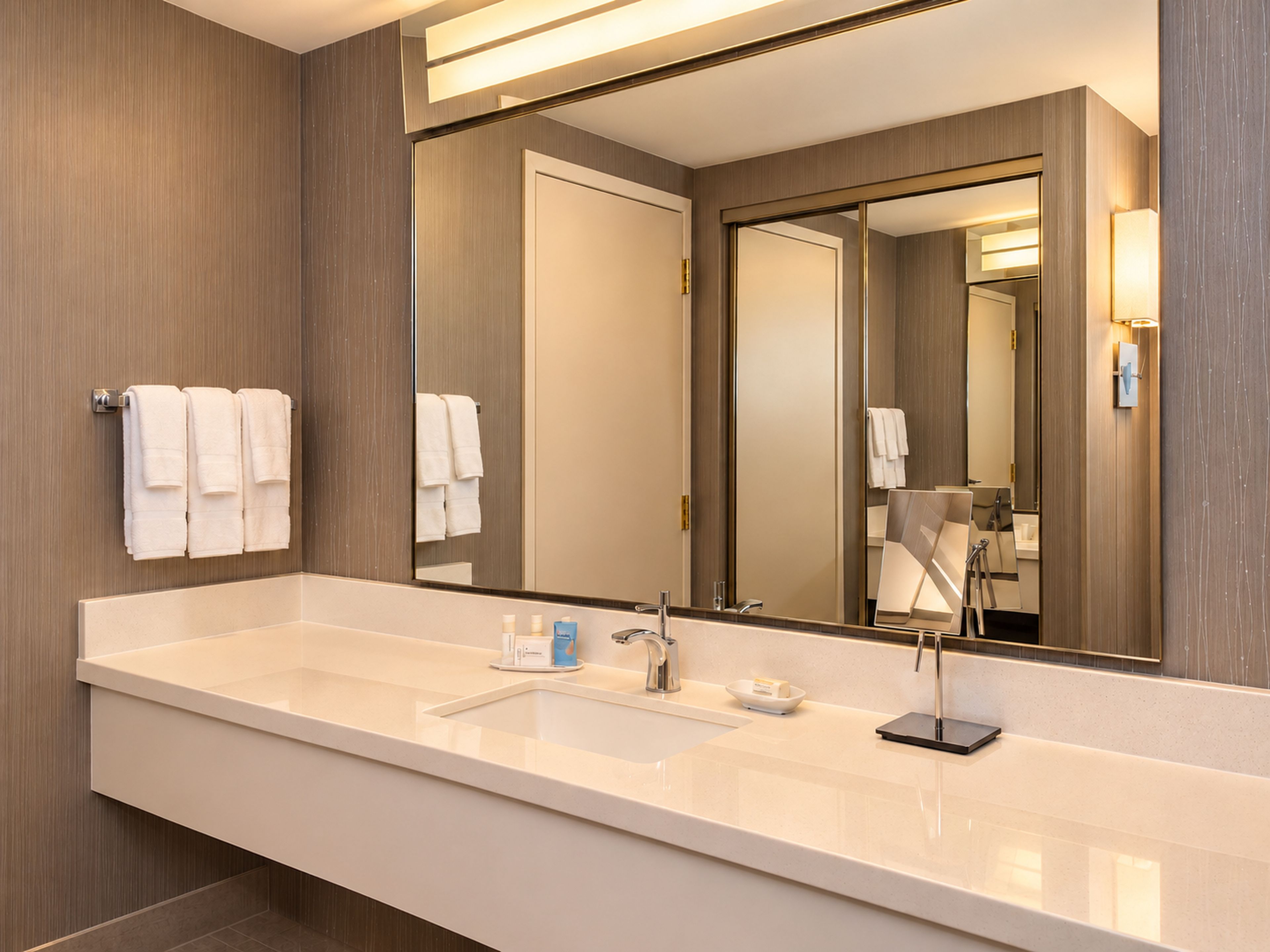 A hotel bathroom with a large mirror, a sink, and a towel rack.
