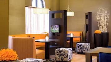 Een moderne hotellobby met zithoeken, een televisie en decoratieve elementen.