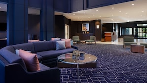 Un hall d’entrée moderne avec un tapis à motifs bleu foncé, un canapé bleu foncé agrémenté de plusieurs coussins, une table basse en verre et un comptoir d’accueil avec des chaises.