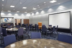 A conference room with round tables and chairs, a projector screen, and a carpeted floor.
