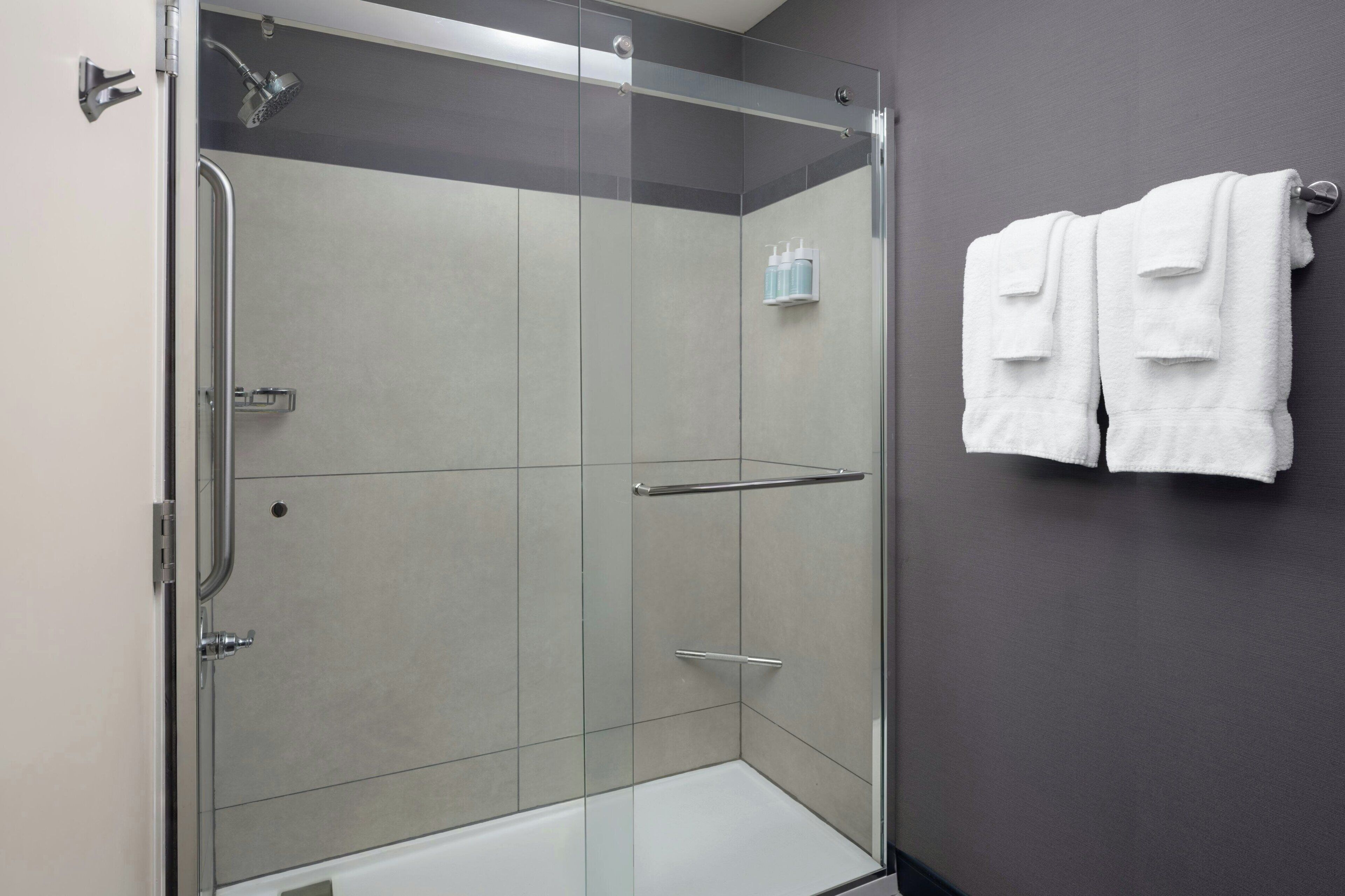 A modern shower with a glass door, a towel rack with two towels, and a small shelf with toiletries.