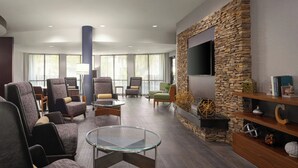 Un moderno vestíbulo de hotel con asientos, una pared de acento de piedra, un televisor de pantalla plana y una chimenea.