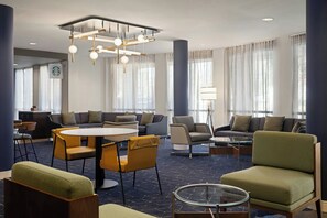 Un hall dâhĂŽtel moderne avec une table ronde, des canapĂ©s, des fauteuils et un coin cafĂ©.