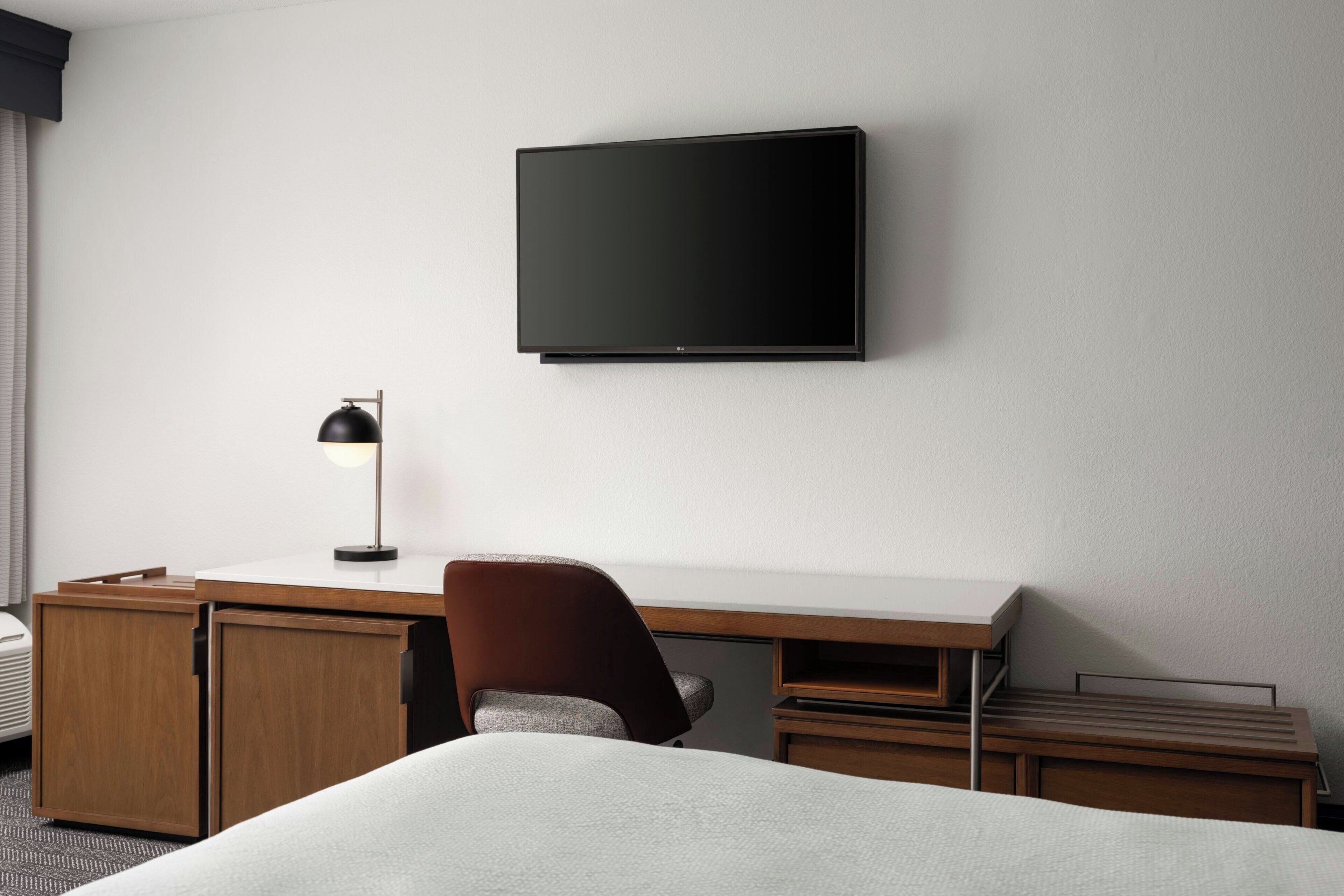 A hotel room with a bed, a desk, a chair, a television, and a lamp.