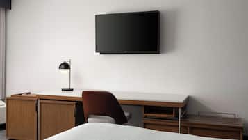A hotel room with a bed, a desk, a chair, a television, and a lamp.
