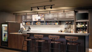 Una zona de bar con taburetes, una pizarra de menú, un refrigerador y un televisor.