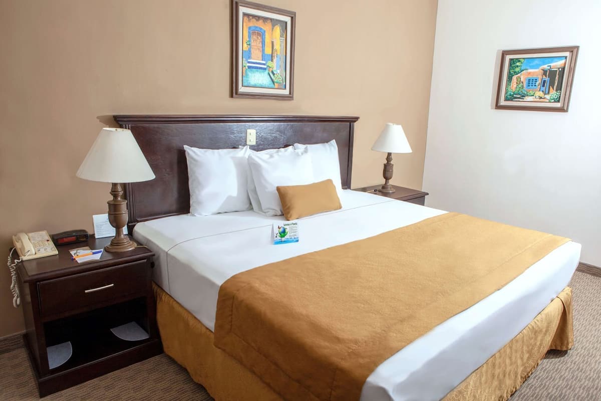 Une chambre d’hôtel avec un lit, deux tables de chevet, une lampe, un téléphone et un tableau encadré au mur.