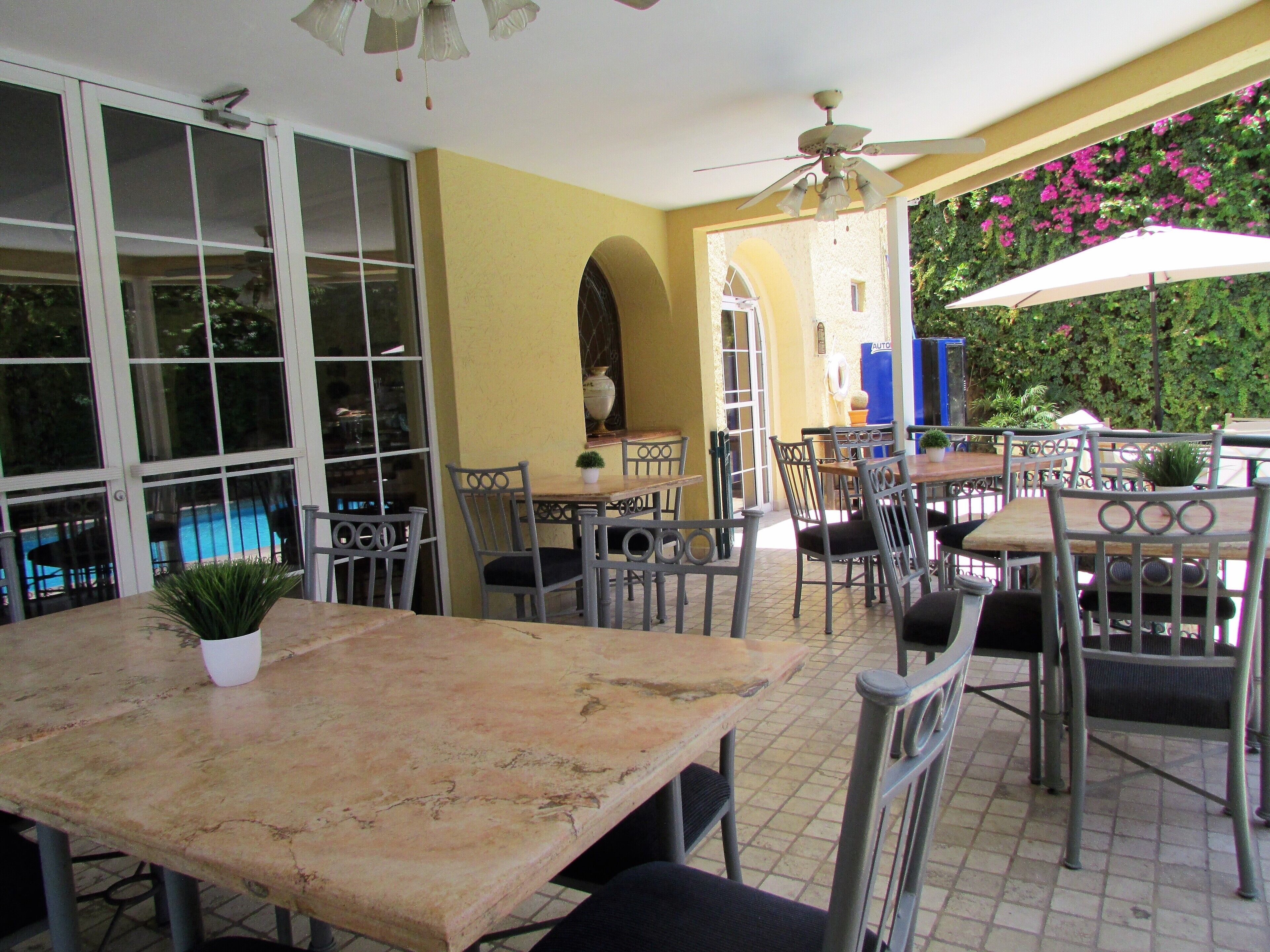 An outdoor patio area with multiple tables and chairs, a ceiling fan, and a view of a swimming pool.