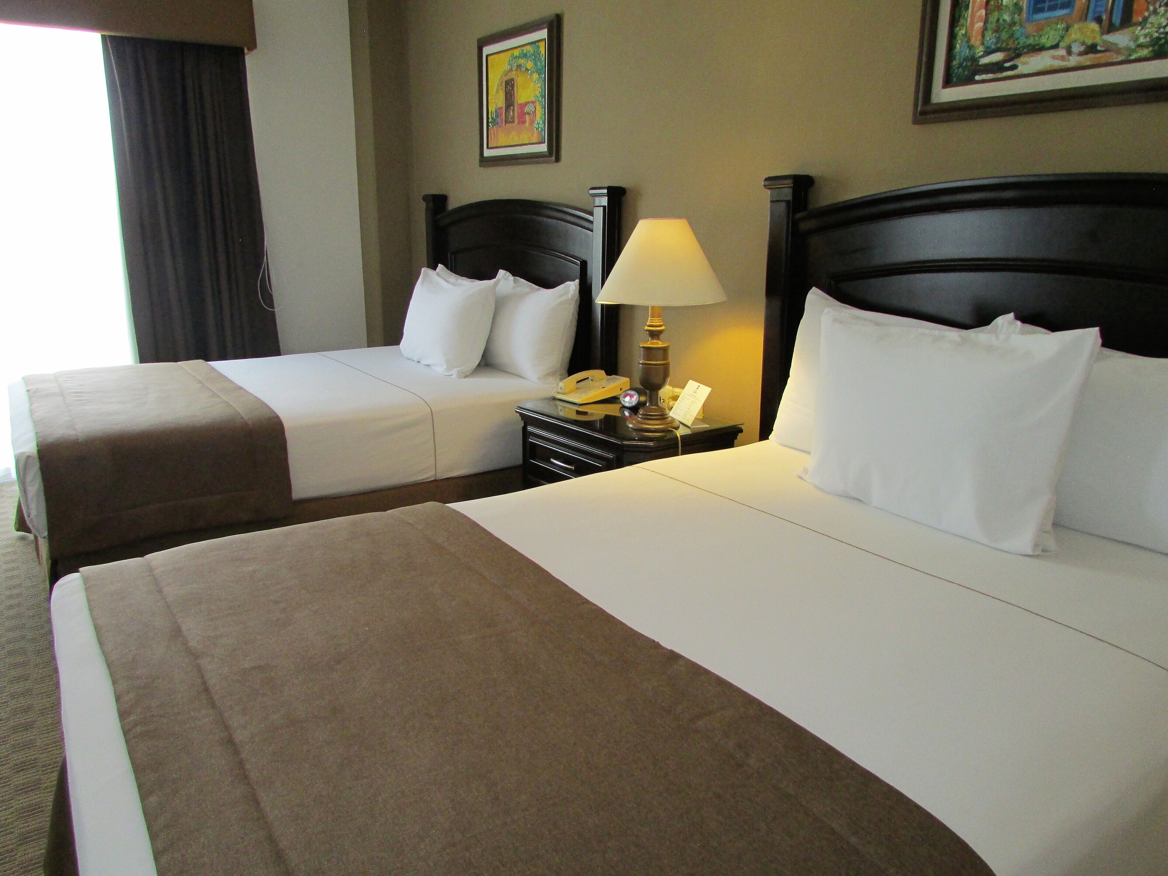 A hotel room with two beds, a nightstand with a lamp, and a painting on the wall.
