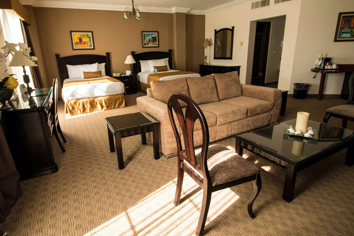 Une chambre d’hôtel dotée d’un lit « king-size », d’un coin salon avec un canapé et des fauteuils, d’une table basse et d’un bureau avec une lampe.