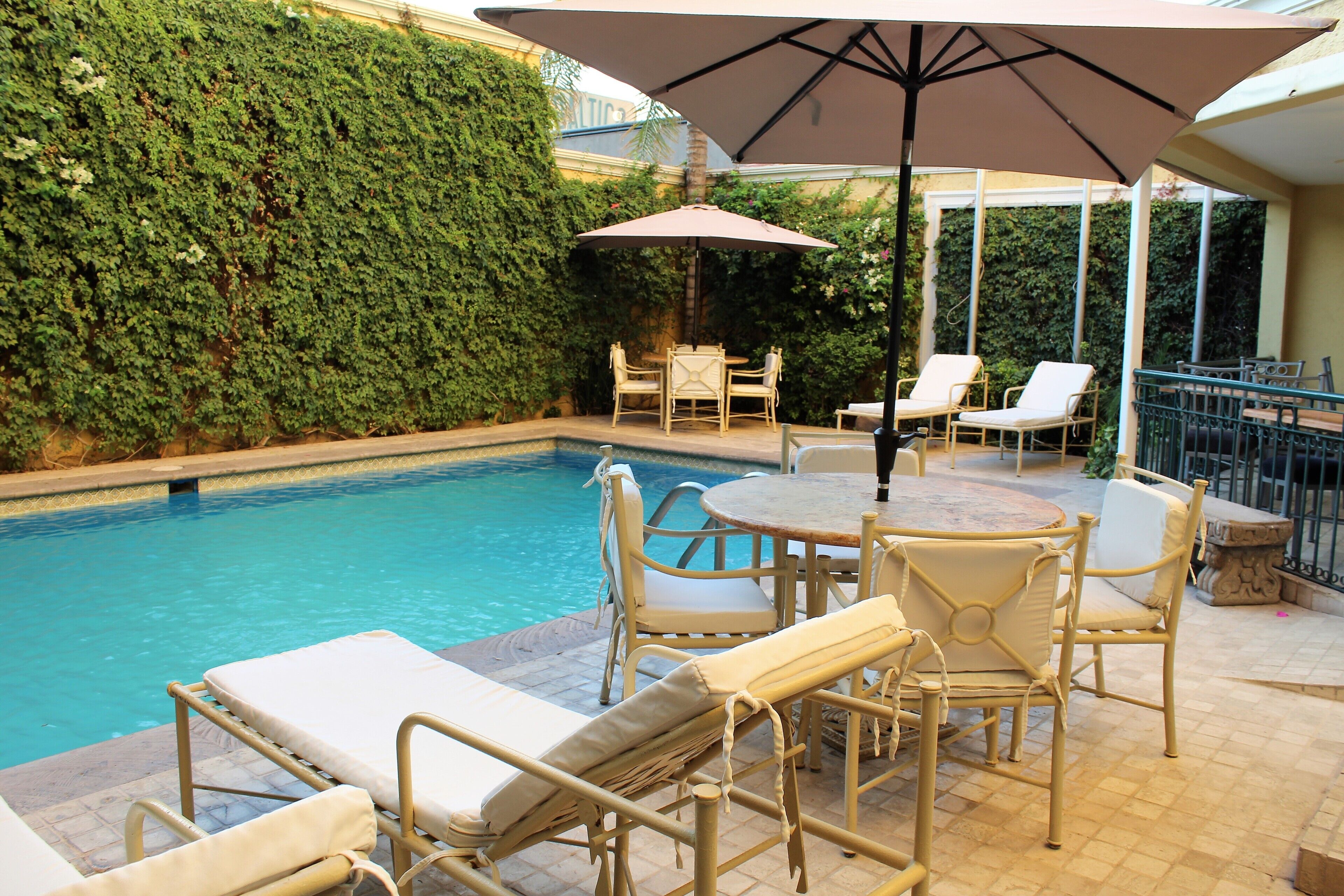 Zona de piscina con sillones de descanso y una mesa bajo una sombrilla, rodeada de un seto.