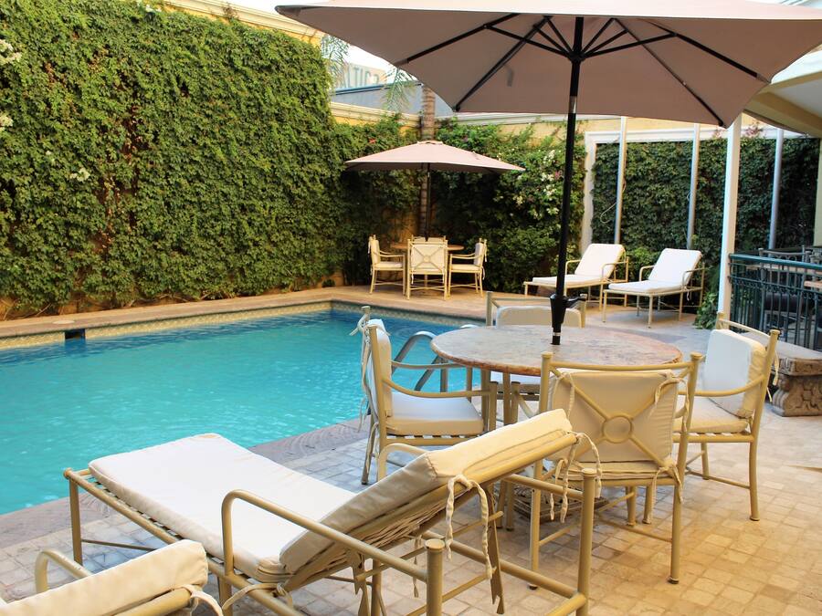 Zona de piscina con sillones de descanso y una mesa bajo una sombrilla, rodeada de un seto.
