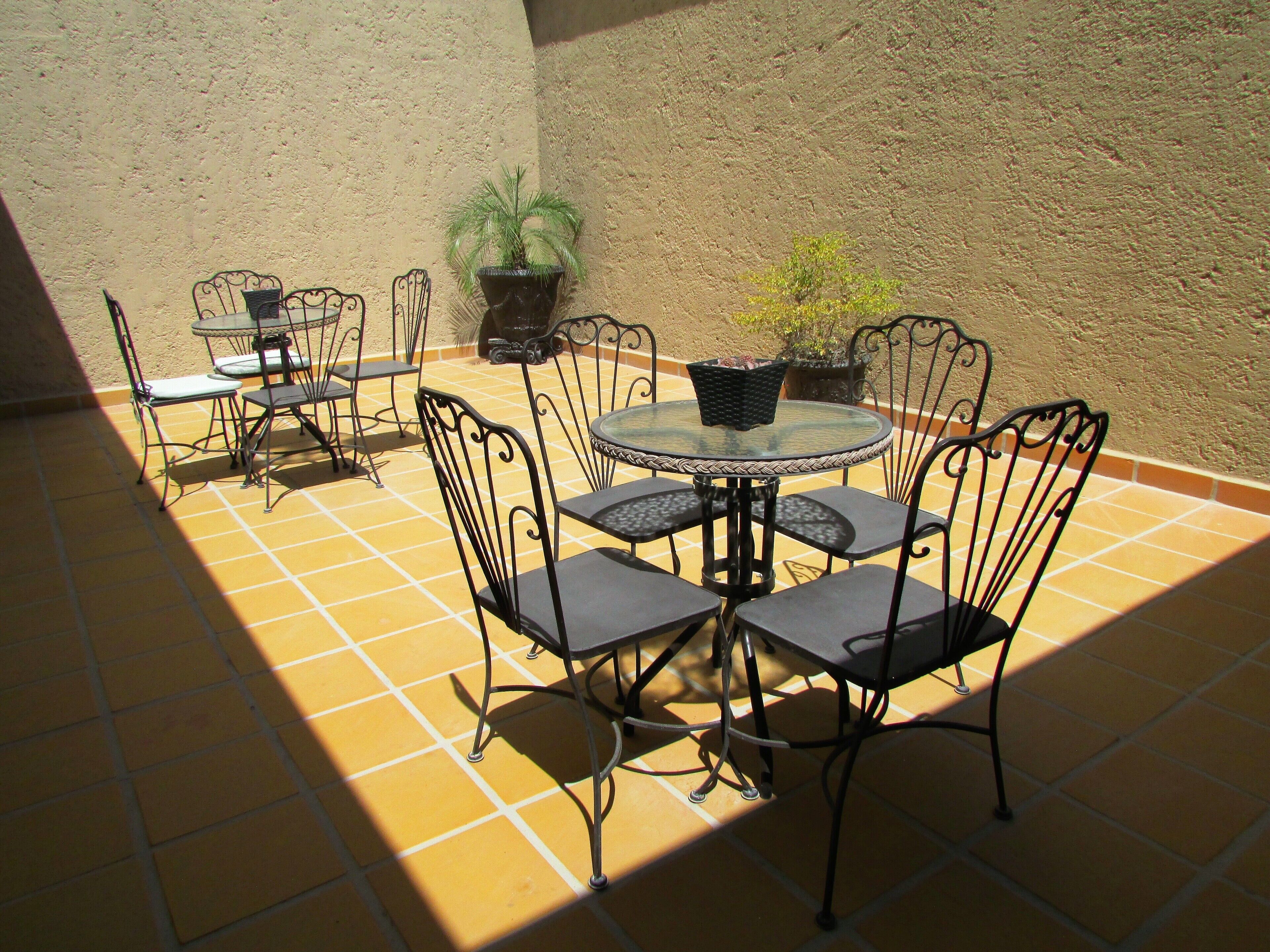 A patio with a round table and four chairs, surrounded by potted plants.
