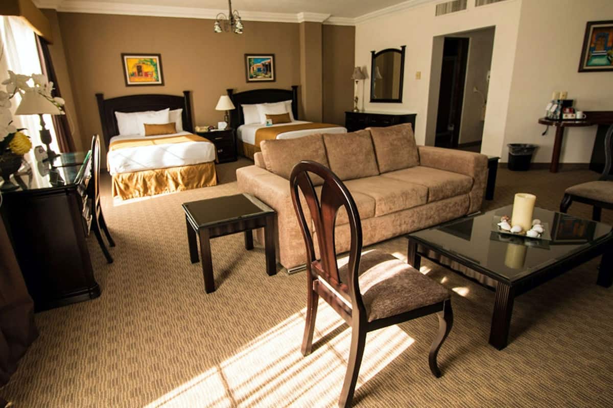 Une chambre d’hôtel avec deux lits, un canapé, une chaise, une table basse et une lampe.