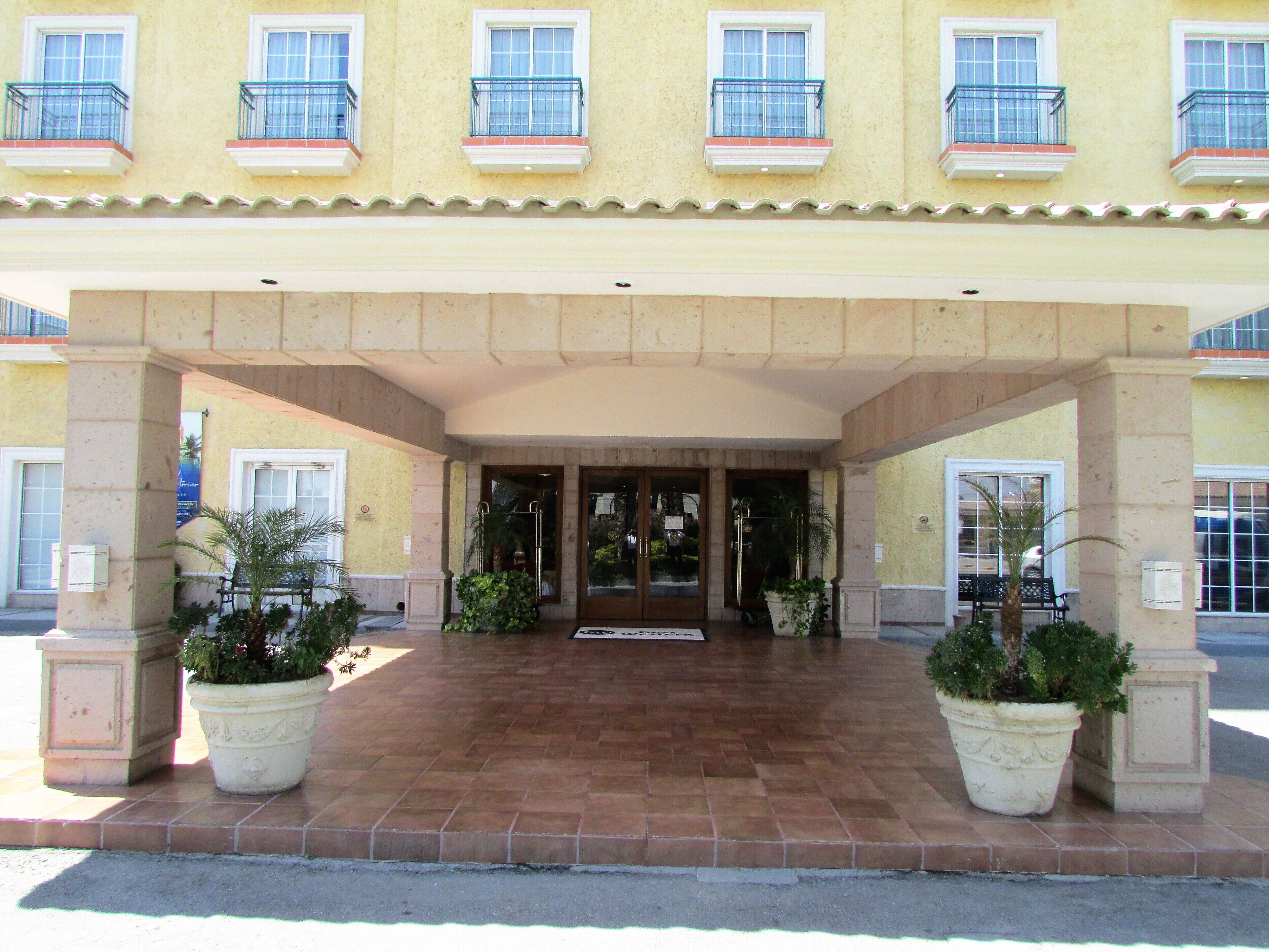 A hotel entrance with a tiled patio, potted plants, and a covered entrance.
