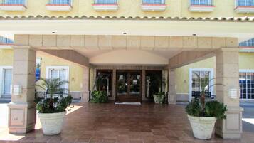 A hotel entrance with a tiled patio, potted plants, and a covered entrance.