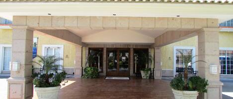 A hotel entrance with a tiled patio, potted plants, and a covered entrance.