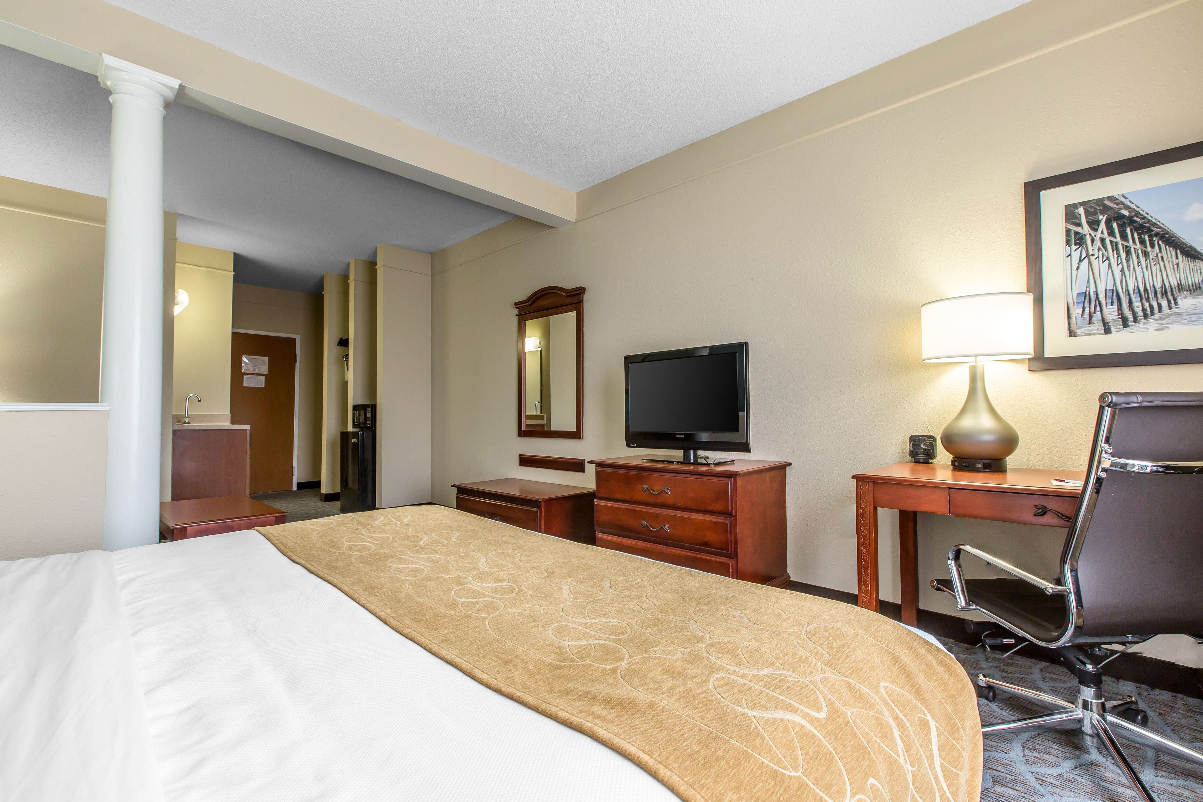 Une chambre d’hôtel avec un lit, un bureau, une chaise, une télévision et un tableau au mur.