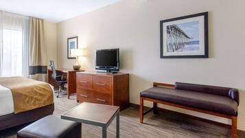 A hotel room with a bed, a desk, a television, a bench, and a framed picture of a pier.