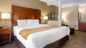A hotel room with a large bed, two bedside lamps, a nightstand, a wooden headboard, and a small table with a lamp.
