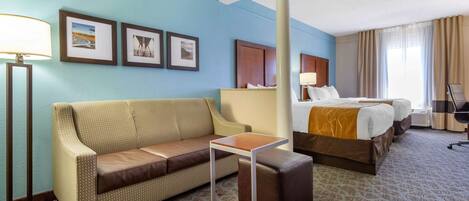 Quarto de hotel com sofá, mesa pequena, cama e mesa de cabeceira.